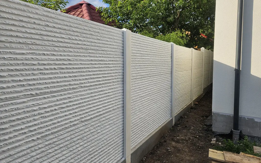 Weißer Betonzaun mit Reliefplatten entlang eines Hauses