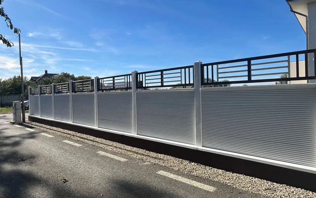 Weißer Betonzaun mit Metallgitter über den Zaunplatten, an einer Straße