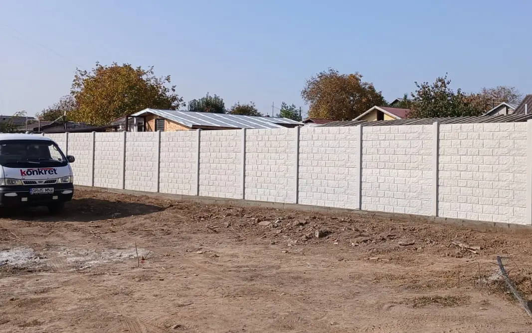 Fahrzeug von Konkret Line neben einem weißen Betonzaun mit Relief in Mauersteinoptik